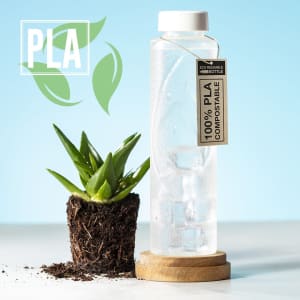 A drink bottle made from clear material, featuring a tag indicating it's 100% compostable, next to a potted plant.