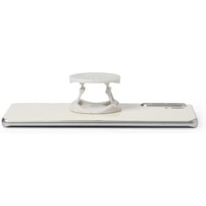 A white phone stand featuring a circular holder, positioned on a sleek silver smartphone. The product includes branding.
