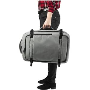 A grey document bag backpack is being held by a person in black pants, featuring multiple compartments and straps.