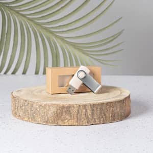 A 16GB USB memory flash drive in silver and white, placed on a wooden slice with a light brown box behind it.