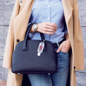 A stylish black handbag is held by a person wearing a striped shirt and beige coat, showcasing a sleek design.