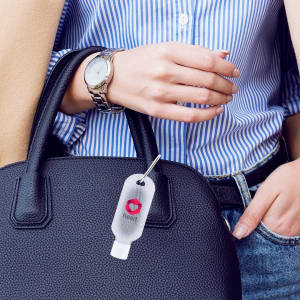 A hand sanitiser bottle attached to a black handbag, featuring a clear design with a white nozzle.