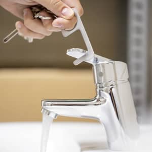 A hand holding a silver keyring anti-contact tool, interacting with a shiny tap while water flows from it.