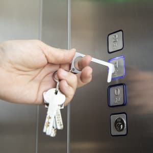 A keyring featuring a silver, anti-contact tool being used to press an elevator button.
