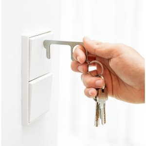 A hand holding a silver keyring tool interacting with a white wall switch, accompanied by a set of keys.