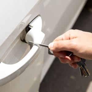 A hand using a silver keyring tool to unlock a white vehicle door, with keys attached.