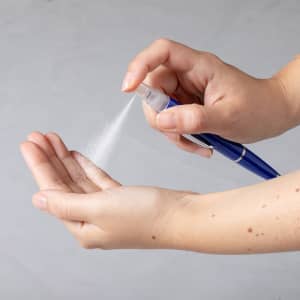 A blue spray pen with a hand demonstrating the spray mechanism, releasing a fine mist.