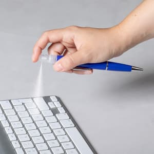 A blue spray pen is being held above a keyboard, dispensing a fine mist.