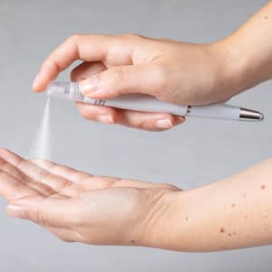A multifunction antibacterial pen in white being used to spray a fine mist from its nozzle onto a hand.