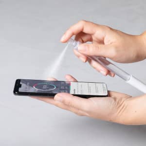 A clear spray pen in hand, misting towards a smartphone screen. The pen features a white design.