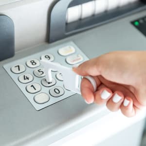 A white antibacterial keyring tool is being used to press buttons on an ATM.