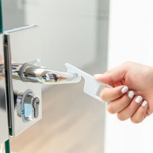 A white antibacterial keyring tool is being used to open a door, featuring a sleek and minimalistic design.