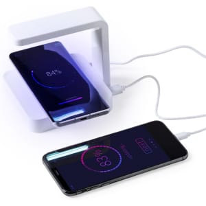 A white UV sterilizer lamp charging two smartphones, displaying battery percentages on their screens.
