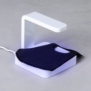 A white UV sterilizer lamp with a sleek design, featuring a black mask resting on its base.