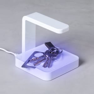 A white UV sterilizer lamp with a minimalist design, featuring keys placed on its illuminated base.