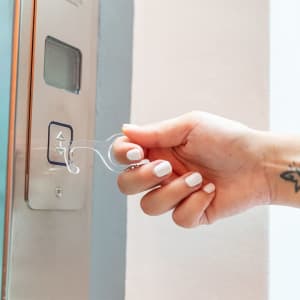 A clear keyring tool is being used to press an elevator button, featuring a minimalist design and an ergonomic grip.