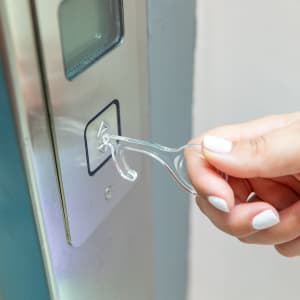 A clear acrylic keyring tool being used to press a button on a panel.