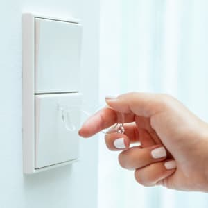 A hand holding a clear keyring with a loop, next to a wall switch. The keyring is designed for contactless operation.