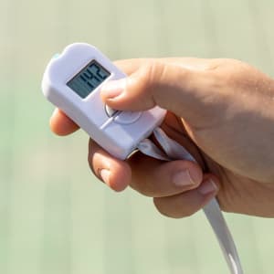 A white digital tally counter held in a hand, featuring a small display and a strap.