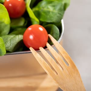 A wooden fork with a red tomato and fresh spinach leaves in a container.