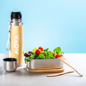 A stainless steel drink bottle with a bamboo finish, accompanied by a silver lunch box filled with fresh salad and utensils.