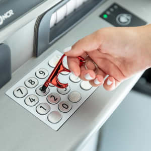 A red anti-contact keyring held above a keypad, designed to avoid direct contact with surfaces.