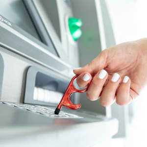 A red anti-contact keyring tool is being used to interact with an ATM keypad.