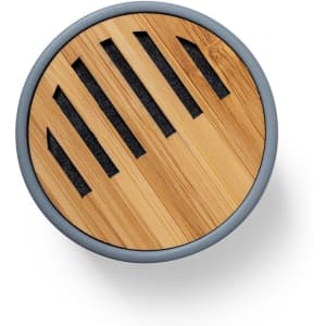 A circular speaker with a bamboo top and grey accents, featuring slotted openings for sound.
