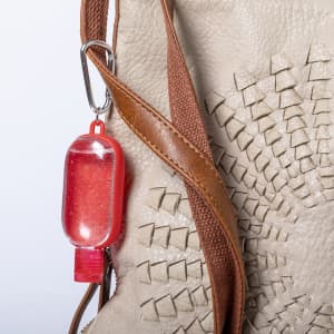 A red hand sanitiser bottle attached to a brown bag, featuring a clear gel inside.