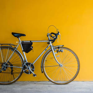 A silver bicycle with a black bike bag attached, set against a vibrant yellow wall.