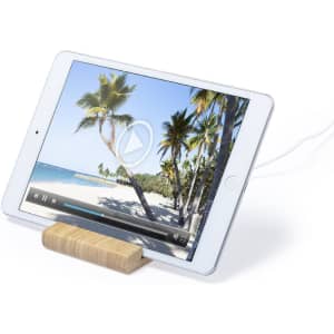 A wireless charger in a sleek design holds a tablet displaying a beach scene, with wooden accents for support.