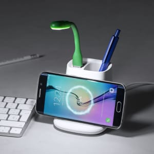 A white multifunction pencil holder with a green light, two pens, and a smartphone. It features a logo.