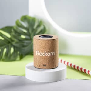 A cork-style speaker in a cylindrical shape, featuring a logo and set against a green and grey backdrop.