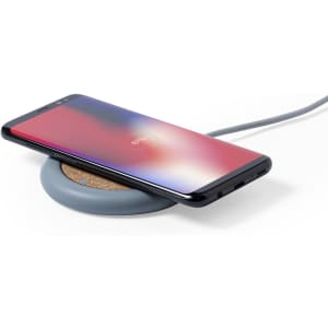 A wireless charger in grey with a cork surface, featuring a smartphone placed on top. The charger has a subtle branding.