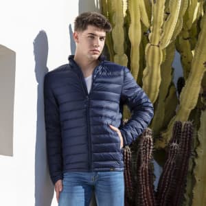 A puffer jacket in navy, featuring a zip closure and a high collar, displayed against a backdrop of cacti.