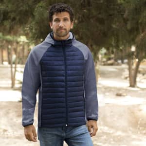 A man wearing a navy blue and grey soft shell jacket with a hood, standing in a natural outdoor setting.