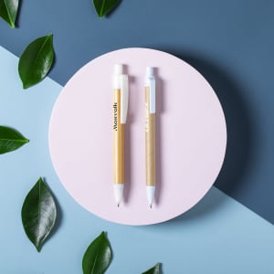 A circular surface displays two pens: one with a white barrel and a gold tip, the other fully white, surrounded by green leaves.