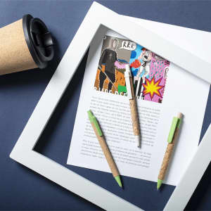 Three Yarden Pens with green accents are placed on a sheet of paper with a frame and a drink cup beside them.