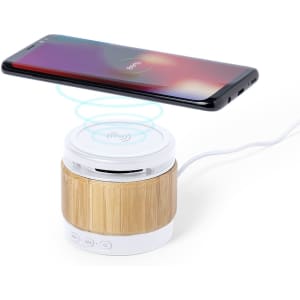 A bamboo and white wireless charger speaker with a smartphone positioned above it, featuring a logo on the speaker.