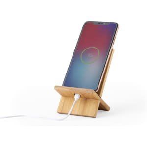 A bamboo phone stand holds a smartphone, displaying a battery charging icon. It features a logo on the base.