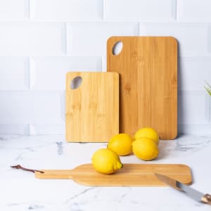 Bamboo chopping boards in two sizes, with three lemons and a knife on a marble countertop.