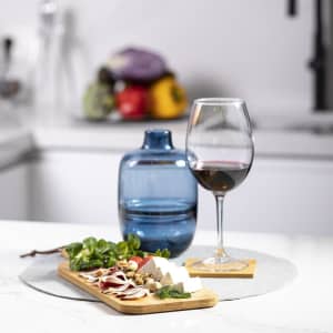 A wooden cutting board featuring cheese and charcuterie, accompanied by a blue drink bottle and a wine glass on a marble surface.