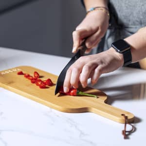 A bamboo cutting board with a hand slicing red chillies, featuring a sleek design and a hanging loop.