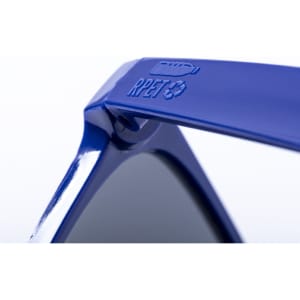 A pair of blue sunglasses with a logo detail on the arm, featuring dark lenses and a sleek design.