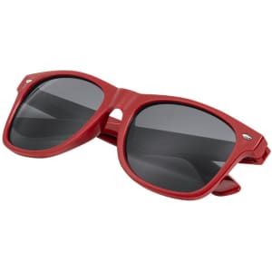 Red sunglasses with dark lenses, featuring a logo on the side, displayed on a flat surface.