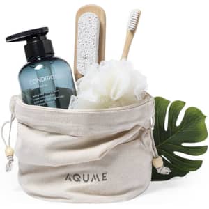 A cream-coloured pouch contains a shampoo bottle, a loofah, a foot file, and a toothbrush, alongside a green leaf.