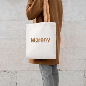 A light-coloured tote bag with brown handles, featuring a logo on the front.