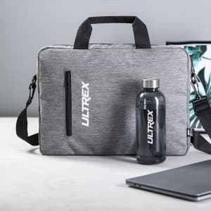 A grey laptop bag with a zippered pocket, a drink bottle, and a laptop on a desk with a plant in the background.