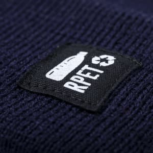 A dark blue beanie featuring a textured pattern and a patch with a logo.