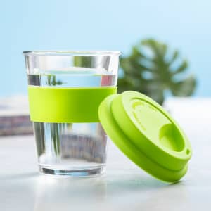 A clear cup with a green silicone sleeve and lid, filled with water, against a light blue background.
